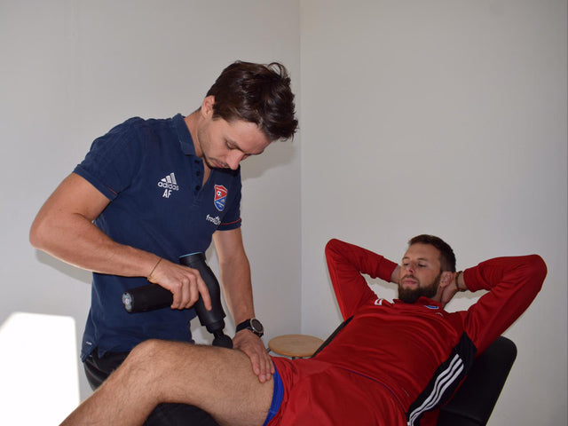 Der Teamphysiotherapeut der SpVgg Unterhaching verwendet die Flow Massagepistole für die Regeneration und Entspannung eines Spielers 